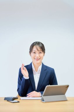 Beyaz bir arkaplan önünde bilgisayar kullanan takım elbiseli bir kadın.