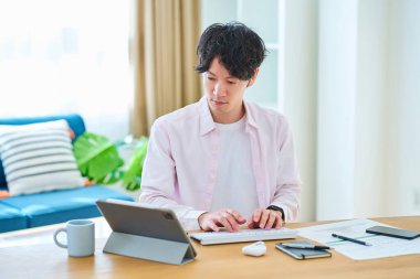 Gündüz vakti odasında bilgisayar kullanan genç bir adam.