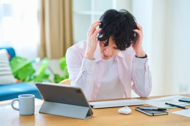 Genç bir adam odasında bilgisayar kullanırken stresli hisseder.