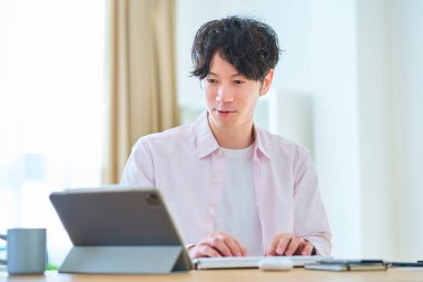 Gündüz vakti odasında bilgisayar kullanan genç bir adam.