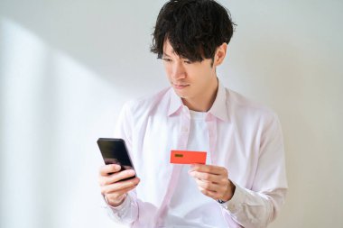 Elinde kart tutan ve beyaz bir arkaplan önünde akıllı telefon kullanan bir adam.