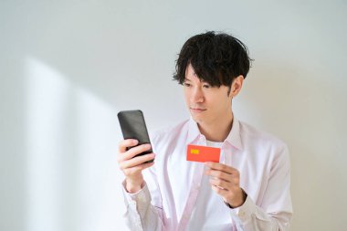 Elinde kart tutan ve beyaz bir arkaplan önünde akıllı telefon kullanan bir adam.