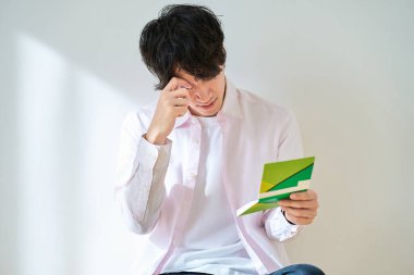 Beyaz bir arkaplan önünde hesap defterine bakan hayal kırıklığına uğramış genç bir adam.