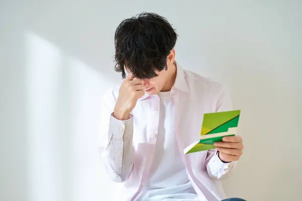 A disappointed young man looking at his passbook in front of a white background
