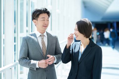 Takım elbiseli bir adam ve kadın koridorda sohbet ediyorlar.