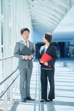 Takım elbiseli bir adam ve kadın koridorda sohbet ediyorlar.