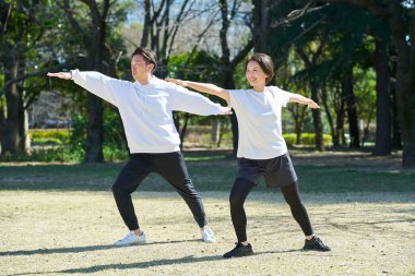 Erkek ve kadın güzel bir günde yan yana yoga yapıyorlar.