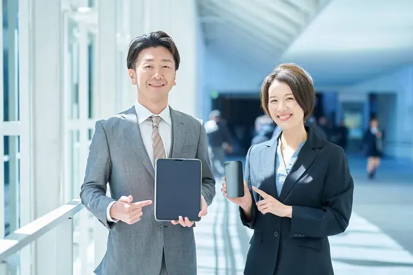stock image A man and a woman in suits holding portable digital communication devices in their hands