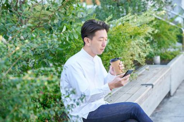Açık havada kahve içerken akıllı telefon kullanan bir adam.