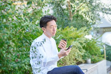 Açık havada kahve içerken akıllı telefon kullanan bir adam.