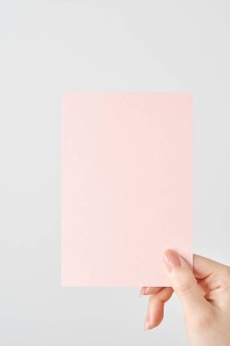 Kadının eli pembe bir kağıt parçası ve beyaz bir zemin tutuyor.