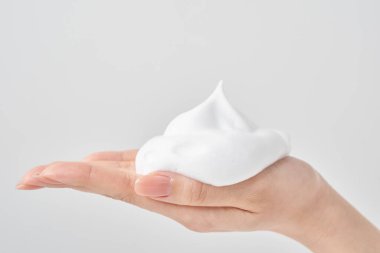 Avuç içine ve beyaz arka planına ince bir köpük yığını yerleştiren bir kadın eli.