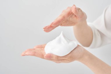 Avuç içine ve beyaz arka planına ince bir köpük yığını yerleştiren bir kadın eli.