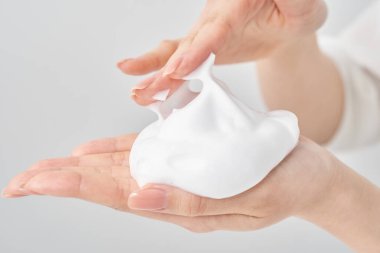 Avuç içine ve beyaz arka planına ince bir köpük yığını yerleştiren bir kadın eli.