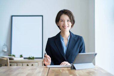 Tablet bilgisayarın önünde takım elbiseli bir kadın oturuyor.