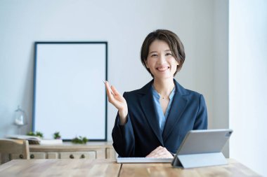 Tablet bilgisayarın önünde takım elbiseli bir kadın oturuyor.