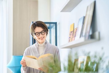 Orta yaşlı bir kadın odasında kitap okuyor.