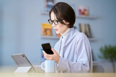 Odada tablet bilgisayar ve akıllı telefon kullanan bir kadın.