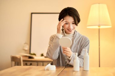 Sıcak ışıklandırmalı bir odada el aynasıyla kendini kontrol eden bir kadın.