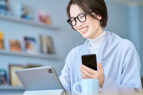 Stock image A woman operating a tablet PC and smartphone in the room