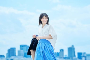 Gündelik giysiler içinde genç bir kadın açık gökyüzü altında çalışacak.