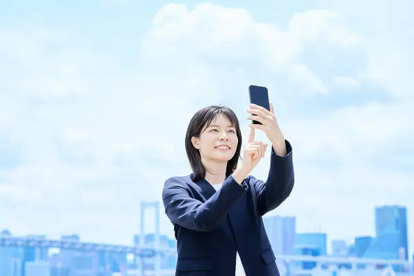 Stock image A young businesswoman operating a smartphone outdoors