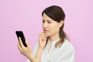 Bir kadın kapalı alanda sorunlu bir ifadeyle akıllı telefon ekranına bakıyor.