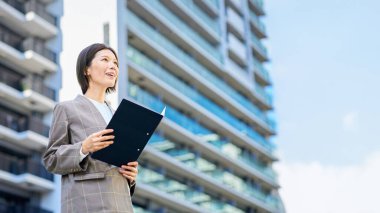 Businesswoman standing in front of an apartment building on fine day clipart