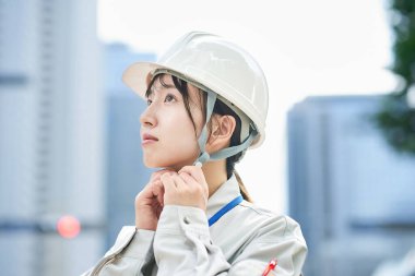 A young woman wearing work clothes and a helmet outdoors clipart