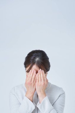 Yüzünü iki eliyle ve beyaz geçmişiyle örten bir kadın.