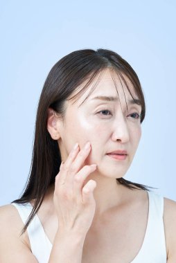 Yüzünde yorgun bir ifade olan orta yaşlı bir kadın cilt bakımı yapıyor ve beyaz bir geçmişi var.