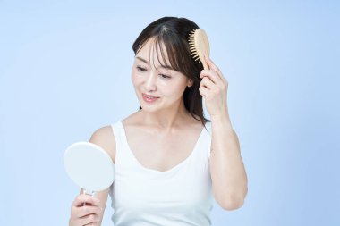 Saçlarını tarayan orta yaşlı bir kadın ve beyaz bir arka plan.