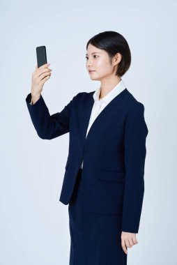 Akıllı telefon ve beyaz arka plan kullanan takım elbiseli bir kadın.