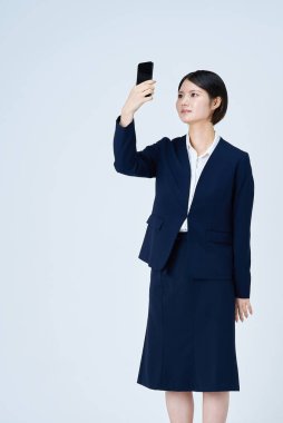Akıllı telefon ve beyaz arka plan kullanan takım elbiseli bir kadın.