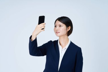 Akıllı telefon ve beyaz arka plan kullanan takım elbiseli bir kadın.