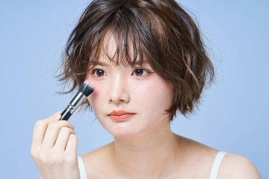 Makyaj yapan ve beyaz arkaplan giyen genç bir kadın.