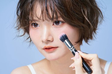 Makyaj yapan ve beyaz arkaplan giyen genç bir kadın.