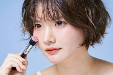 Makyaj yapan ve beyaz arkaplan giyen genç bir kadın.