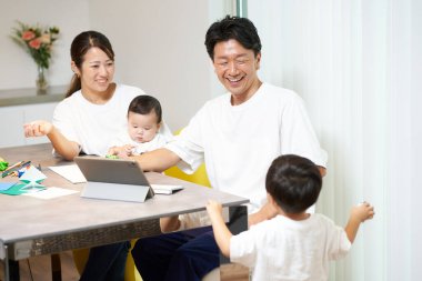 Ailesi yakınlarda oynarken oturma odasında bilgisayar kullanan bir baba.