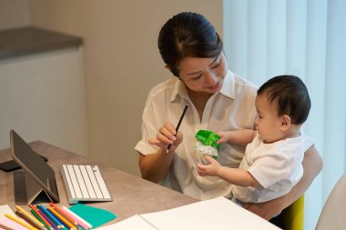 Bir kanepede uzaktan çalışan annesinin yanında oynayan bir çocuk.
