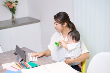 Bir kanepede uzaktan çalışan annesinin yanında oynayan bir çocuk.