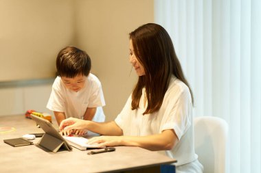 Bir odada uzaktan çalışan annesinin yanında oynayan bir çocuk.