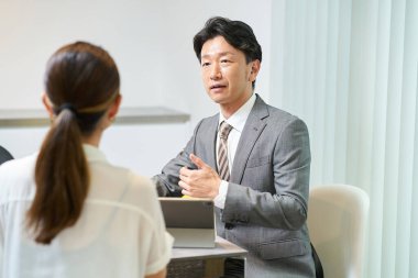 Takım elbiseli bir adam içeride bir kadınla konuşuyor.