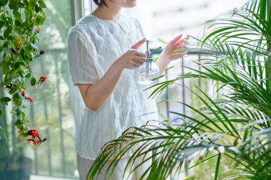 Odasında saksı çiçeği sulayan orta yaşlı bir kadın.