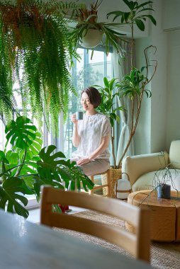 Etrafı saksılarla çevrili orta yaşlı bir kadın dinleniyor.