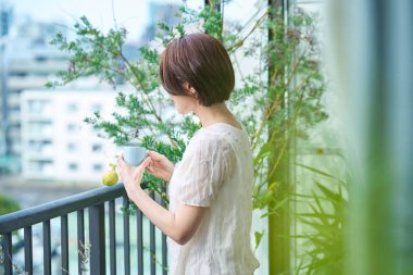 Balkonda bir kupa tutan rahat bir yüzü olan bir kadın.