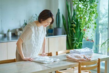 Orta yaşlı bir kadın oturma odasında çamaşır katlıyor.
