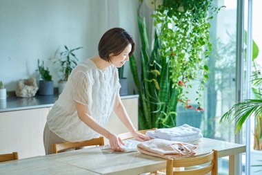 Orta yaşlı bir kadın oturma odasında çamaşır katlıyor.