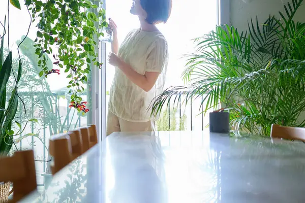 Odasında saksı çiçeği sulayan orta yaşlı bir kadın.