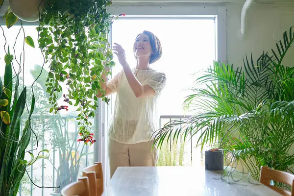 Odasında saksı çiçeği sulayan orta yaşlı bir kadın.